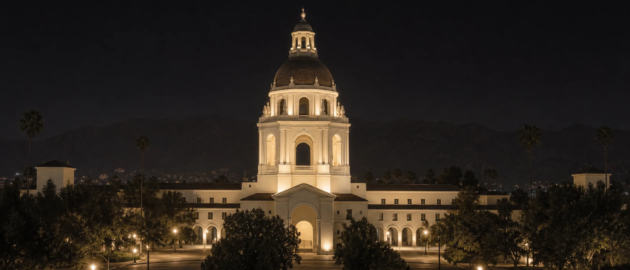 Pasadena City Hall illuminated at blue hour with the San Gabriel Mountains behind it.