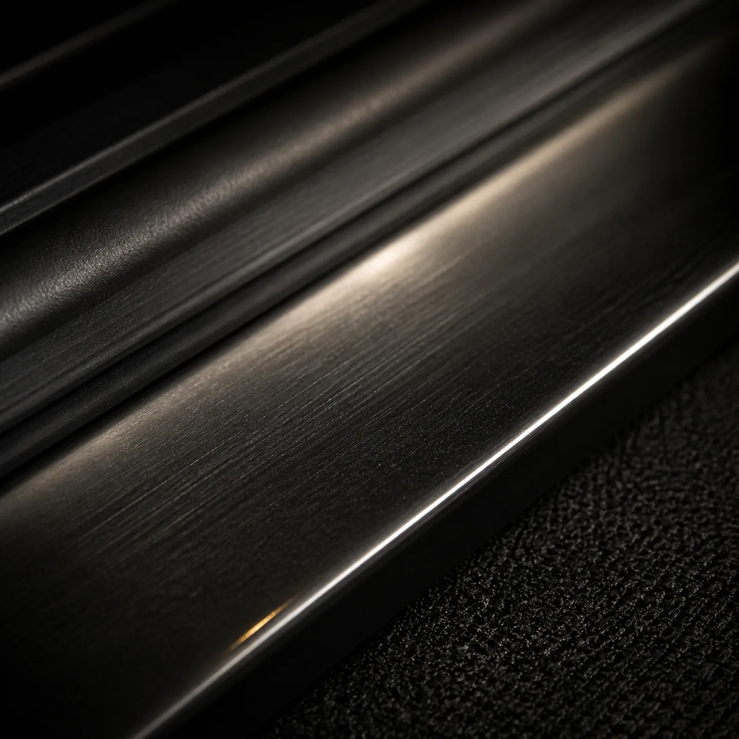 A brushed metal door sill plate with a bright edge line, next to ribbed carpet flooring.